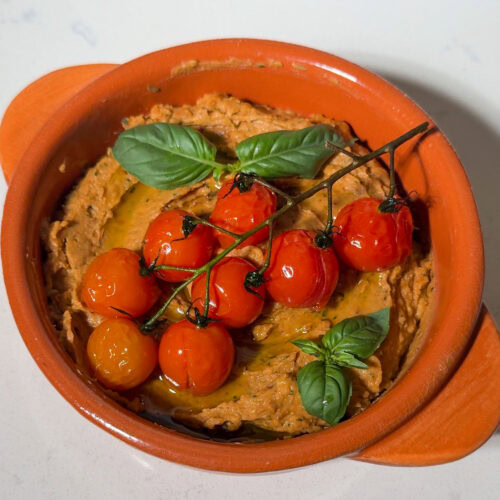 Bowl full of basil tomato white bean dip, topped with roasted tomatoes and basil