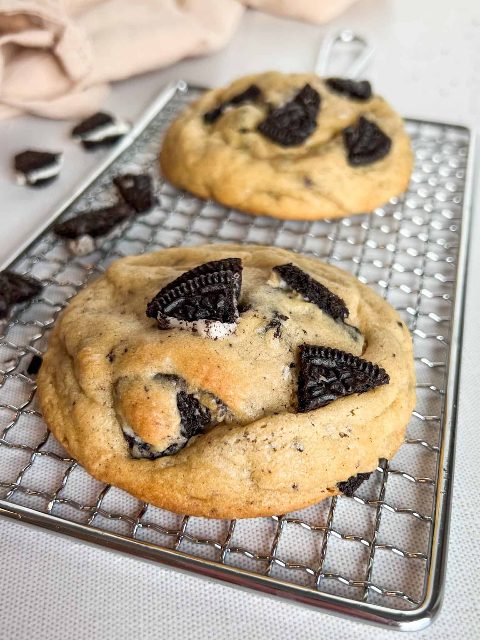 Oreo Cheesecake Cookies (Stuffed!) 10 Two baked Oreo cheesecake cookies sitting on a cooling rack with some crumbled Oreos on the side