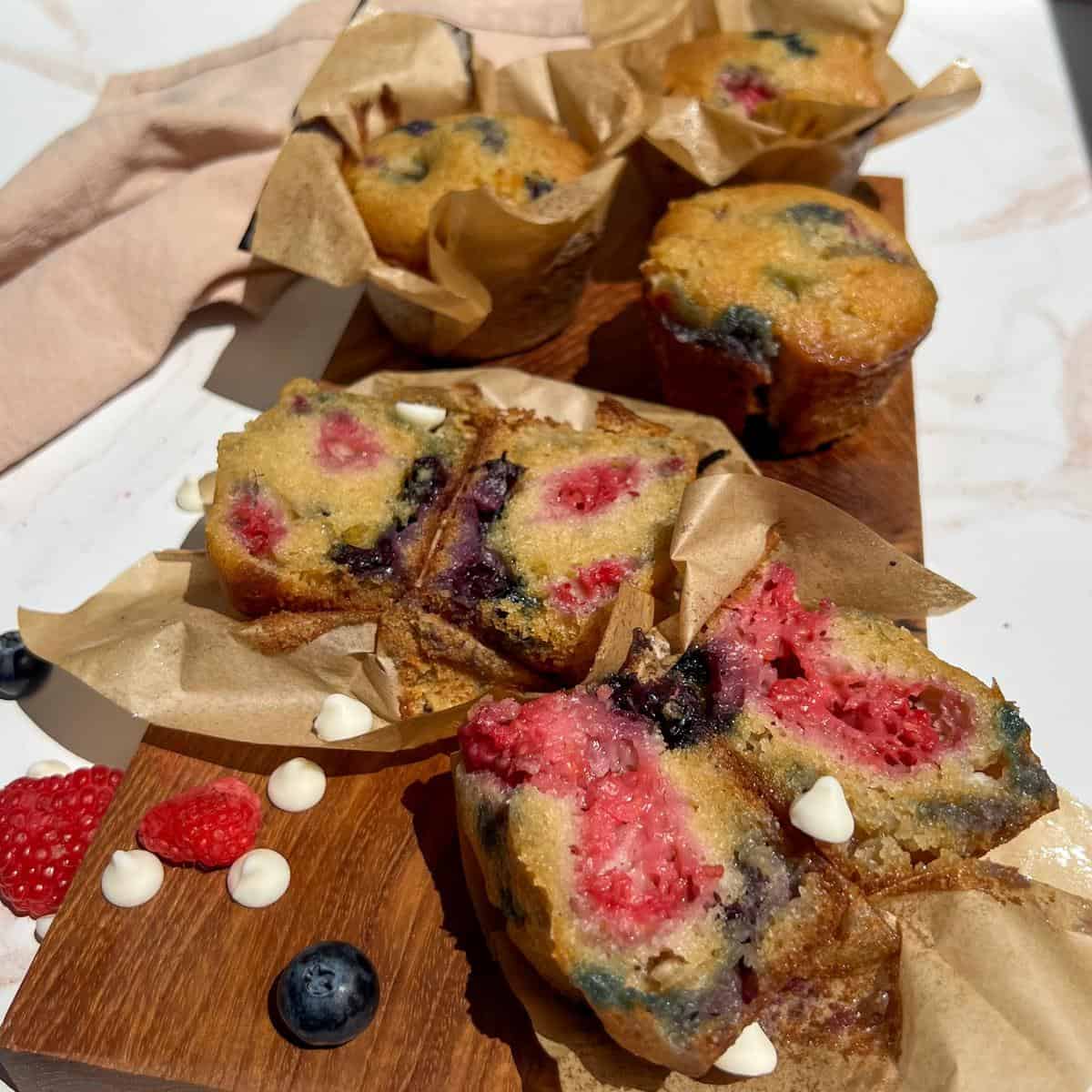 Raspberry Blueberry White Chocolate Muffins laid out on a board in the sun