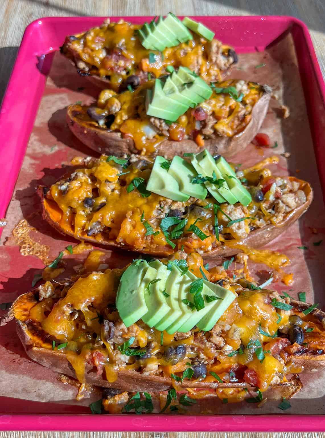Pan of taco turkey stuffed sweet potato boats with melted cheese and avocado on top