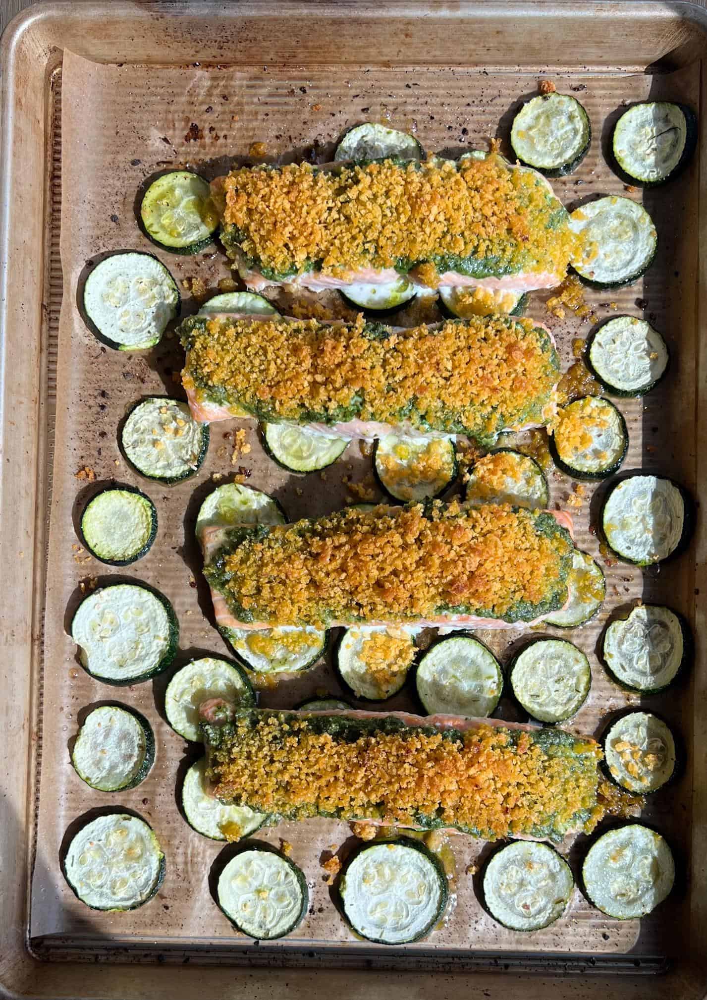 cooked salmon with pesto and lemon crust on the sheet pan over a bed of zucchini