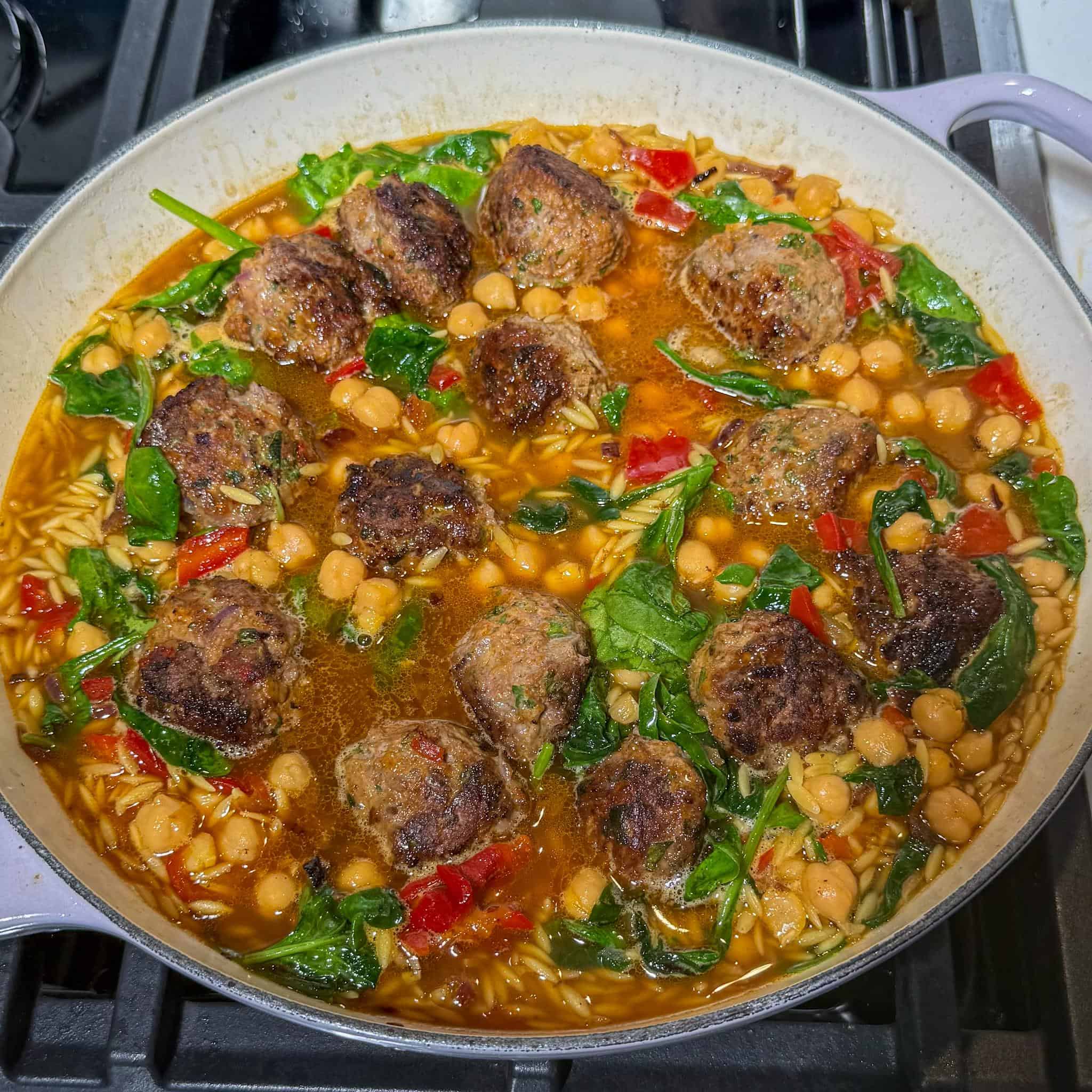 Harissa Lamb Meatballs with Orzo 7 Skillet full of partially cooked harissa lamb meatballs in the uncooked orzo with broth, ready to be placed in the oven