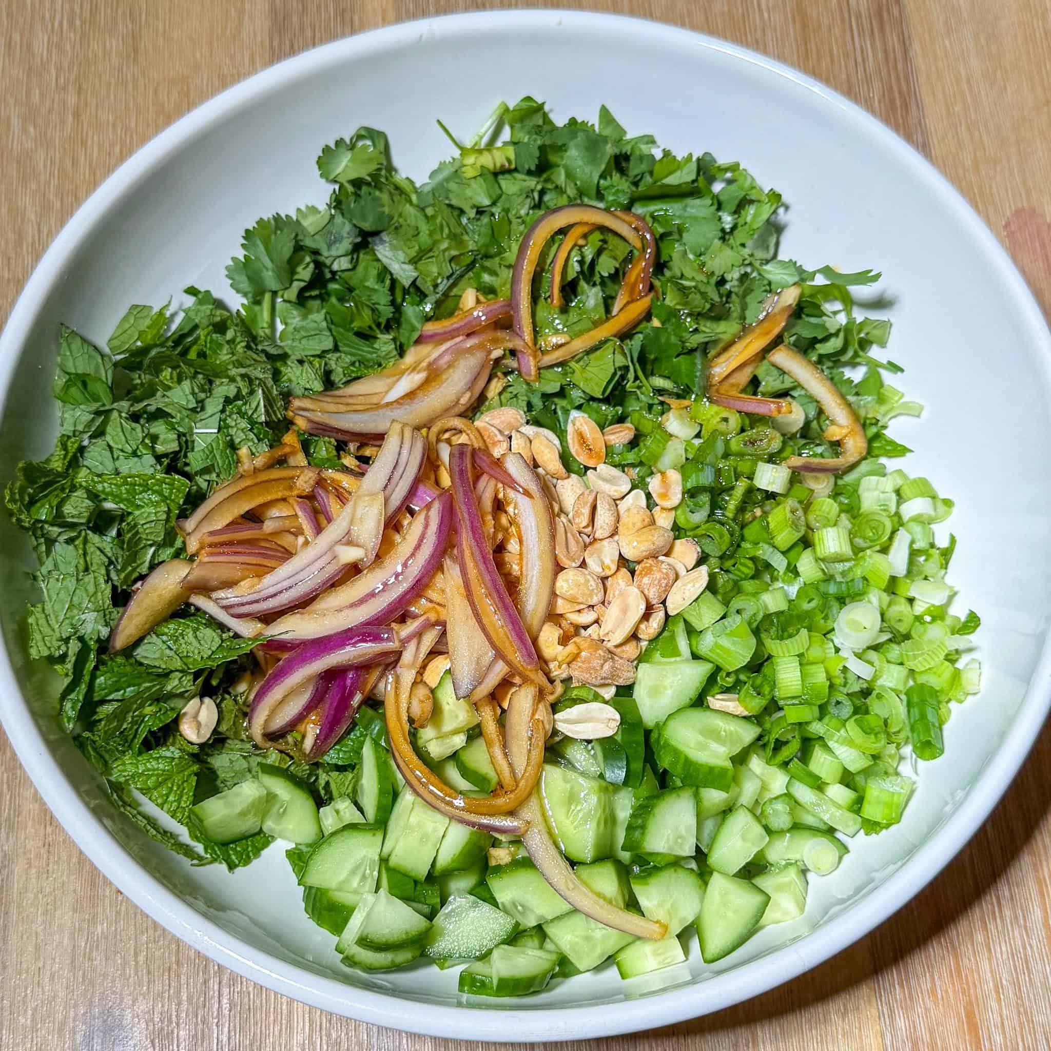 Thai Crispy Rice Salad 4 Herbs, scallions, cucumbers, peanuts, red onions, garlic, and sauce in a bowl.
