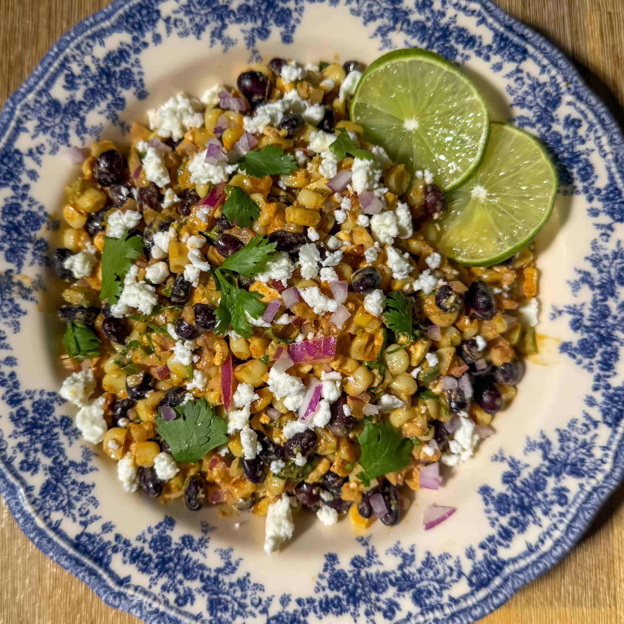 Black bean, corn, and feta dip served in a pretty plate with a few lime wedges as garnish