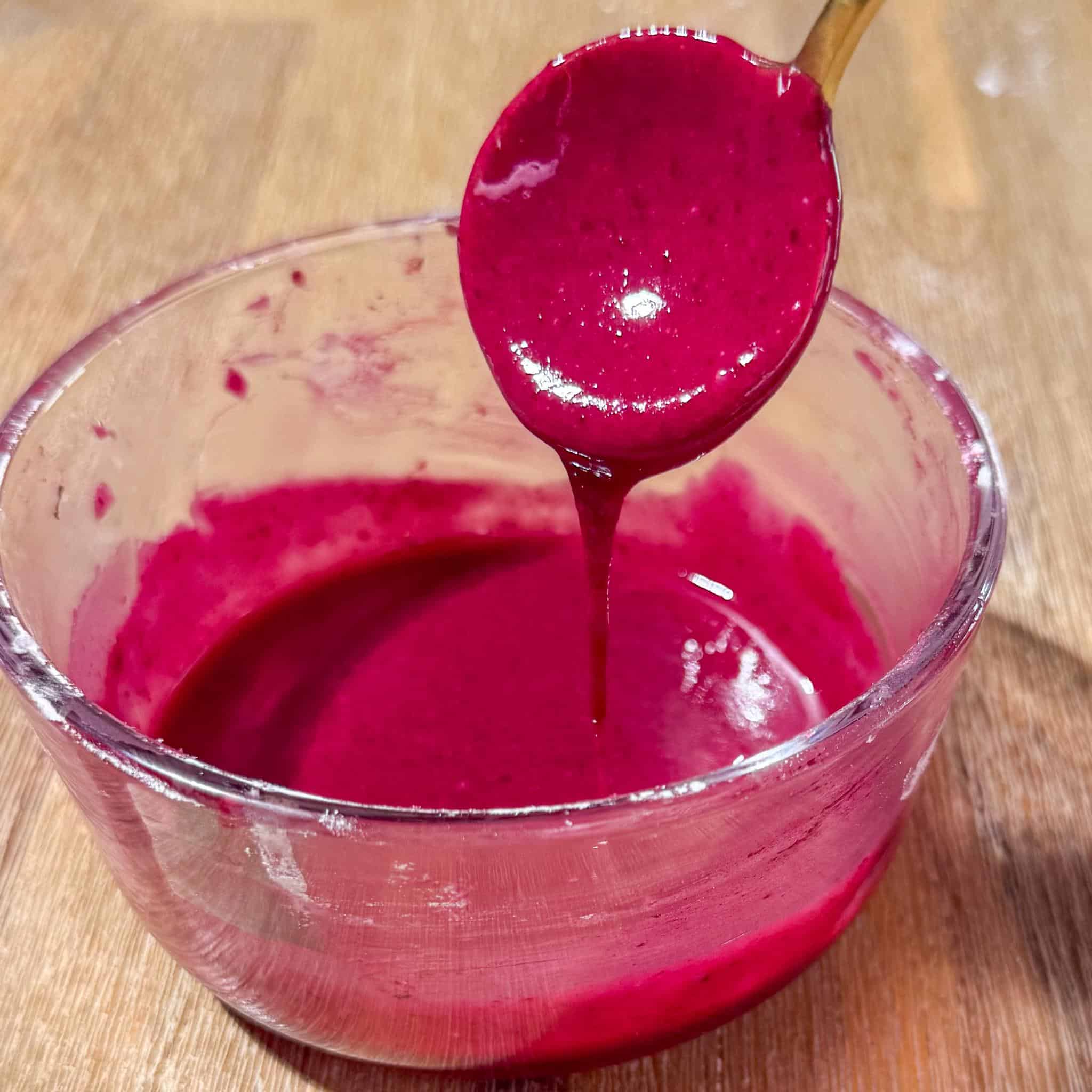 Blueberry Lemon Poppyseed Muffins 7 Magenta blueberry lemon glaze in a small glass bowl with a spoon pouring some down