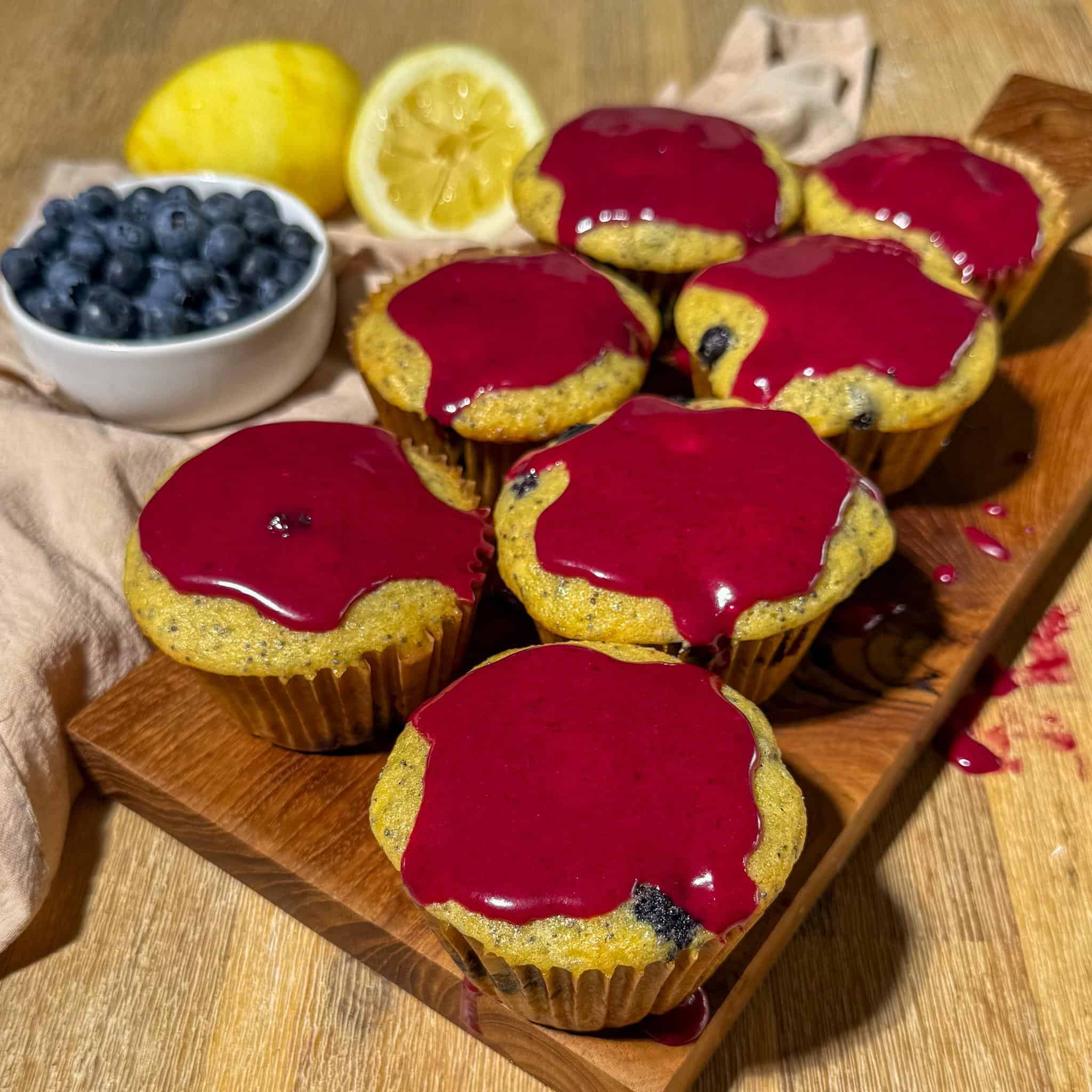 Blueberry Lemon Poppyseed Muffins 3 Glazed blueberry lemon poppyseed muffins on a serving board