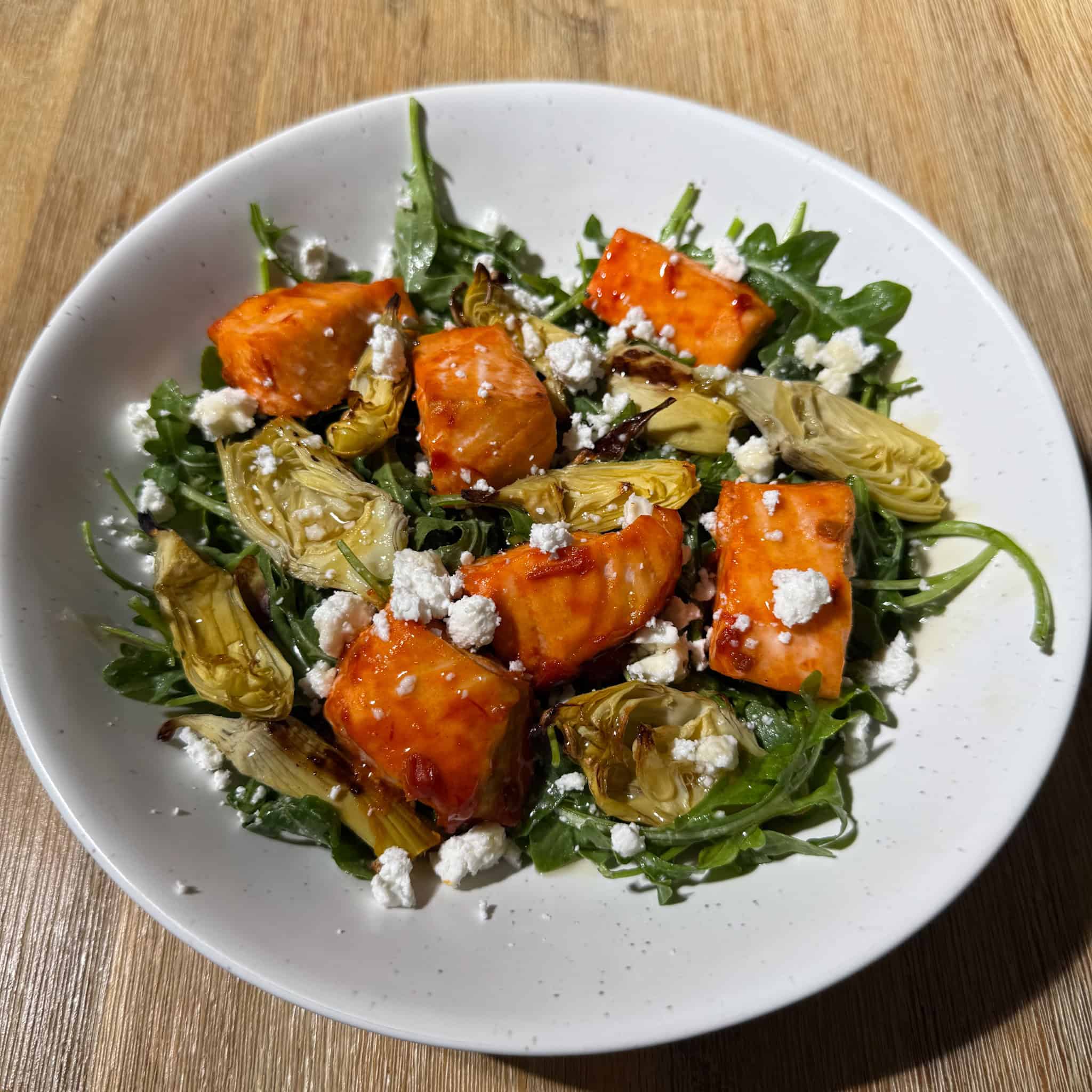 Best harissa honey salmon bites in the oven with artichokes, feta, honey over a bed of arugula salad
