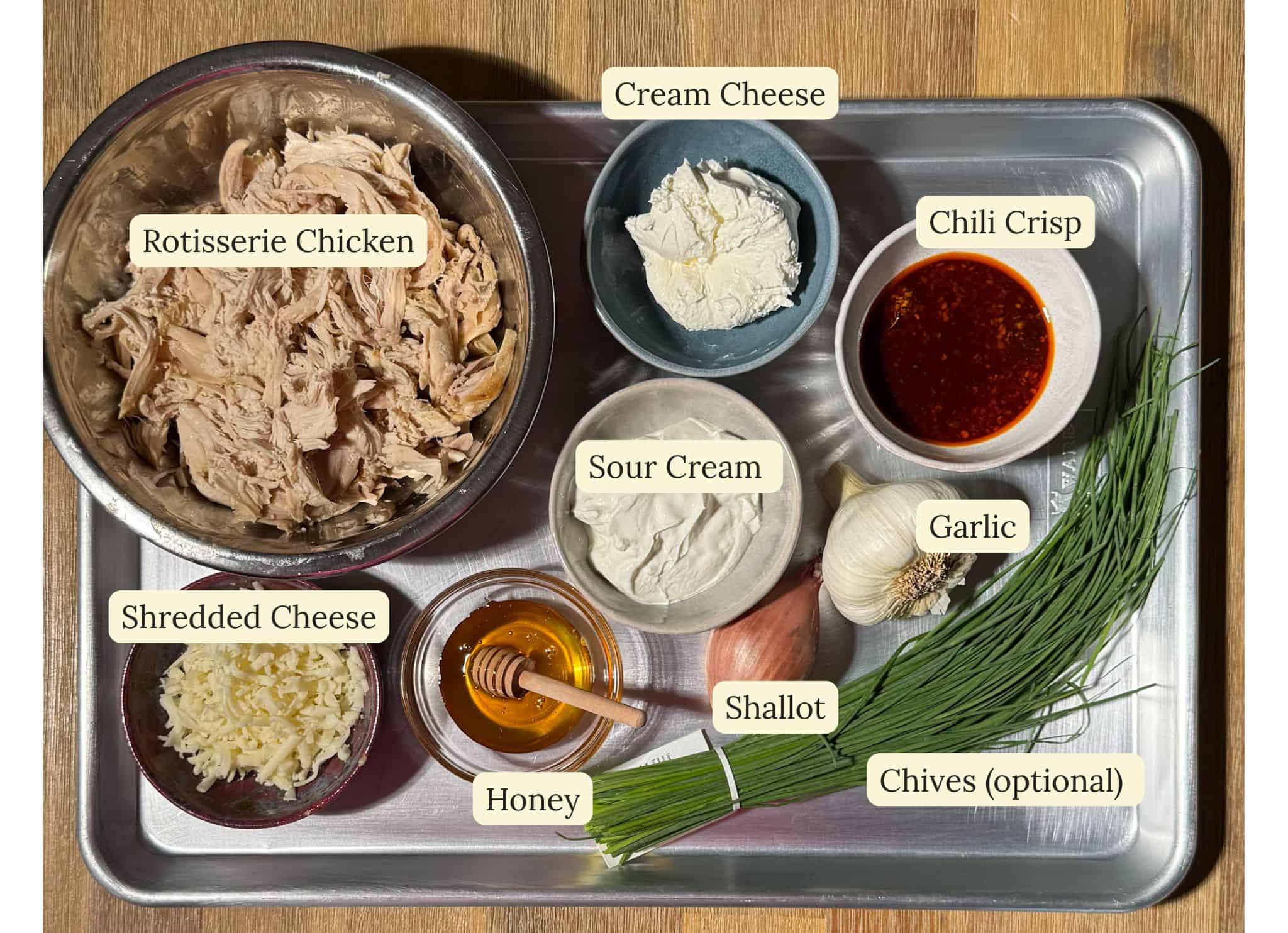 Cheesy Chili Crisp Honey Chicken dip 3 Ingredients for cheesy chili crisp honey chicken dip laid out on a tray and labeled.