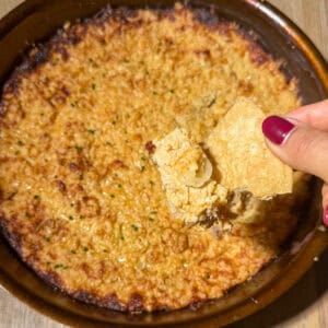 Cheesy Chili Crisp Honey Chicken dip 5 Best cheesy chili crisp honey chicken dip served in a cast iron skillet with a hand holding a chip topped with warm dip