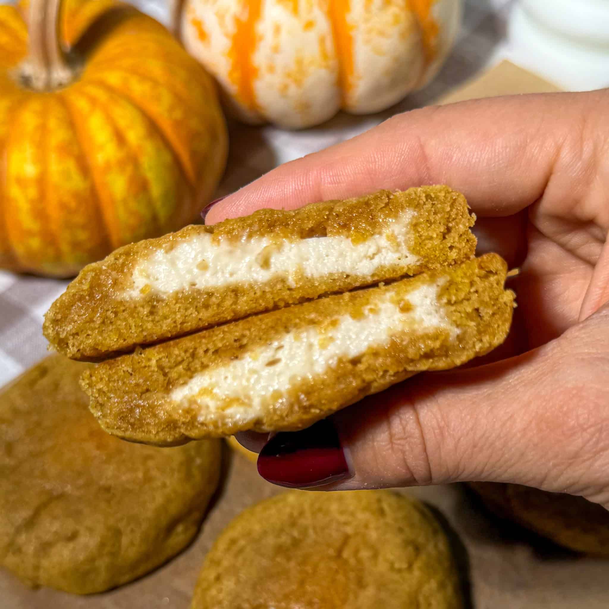 Pumpkin Chai Cheesecake-Stuffed Cookies 2 Gooey pumpkin cream cheese filled cookies on a hand, fall themed snacks with pumpkins in the background, perfect for autumn treats.