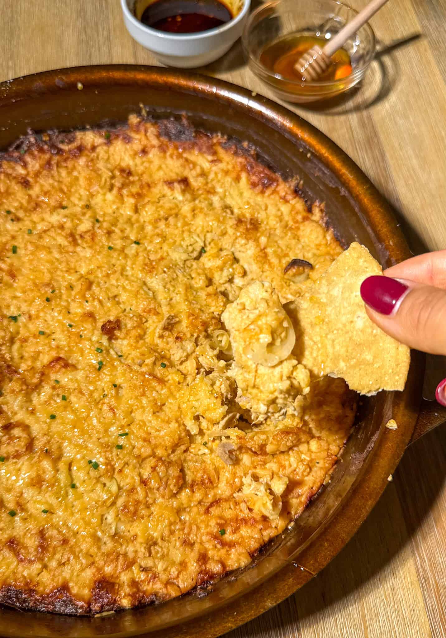 Cheesy Chili Crisp Honey Chicken dip 2 Chili crisp honey chicken dip serve on a table with a chip holding some dip on top and garnish in the background.