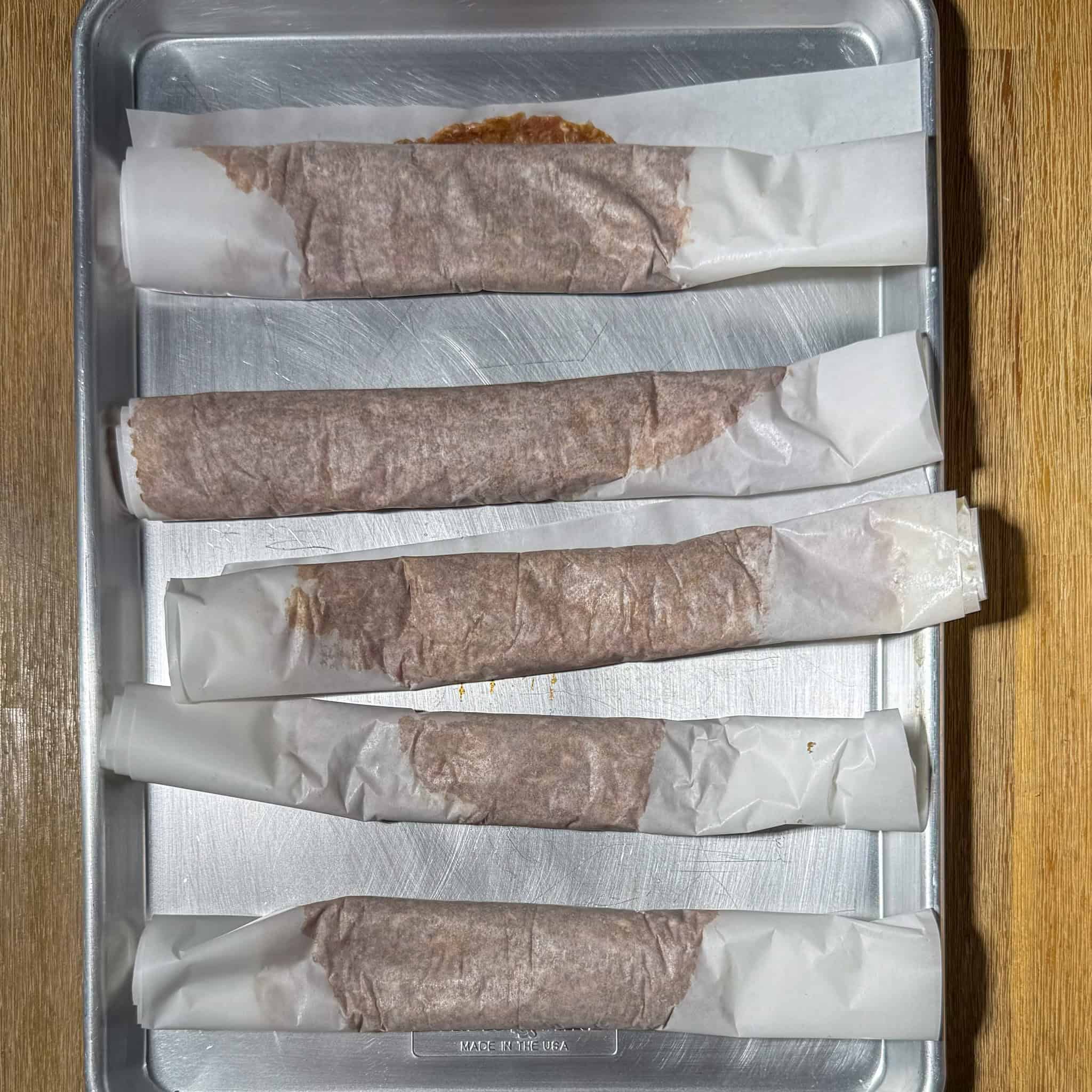 Five rolls of parchment paper wtih meat mixture rolled up thin.