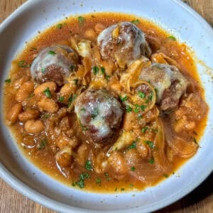 French onion meatballs and beans with broth in a bowl topped with cheese and herbs