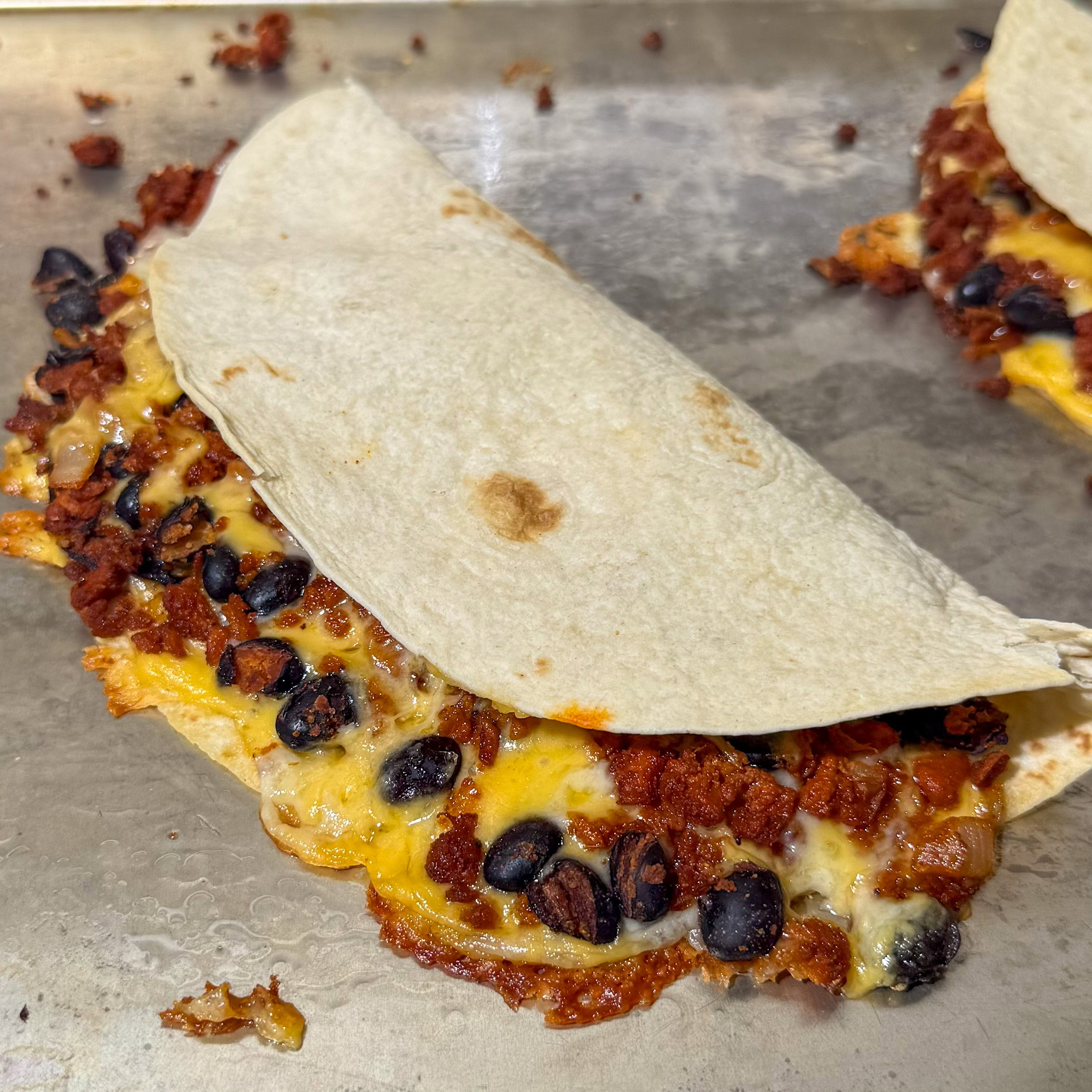 Baked black bean and soyrizo taco without any garnish, with crispy cheese oozing out